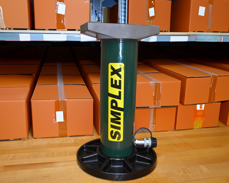 A construction worker wearing a hard hat, safety vest, and tool belt stands confidently next to a yellow featherlite ladder in a bright indoor setting.