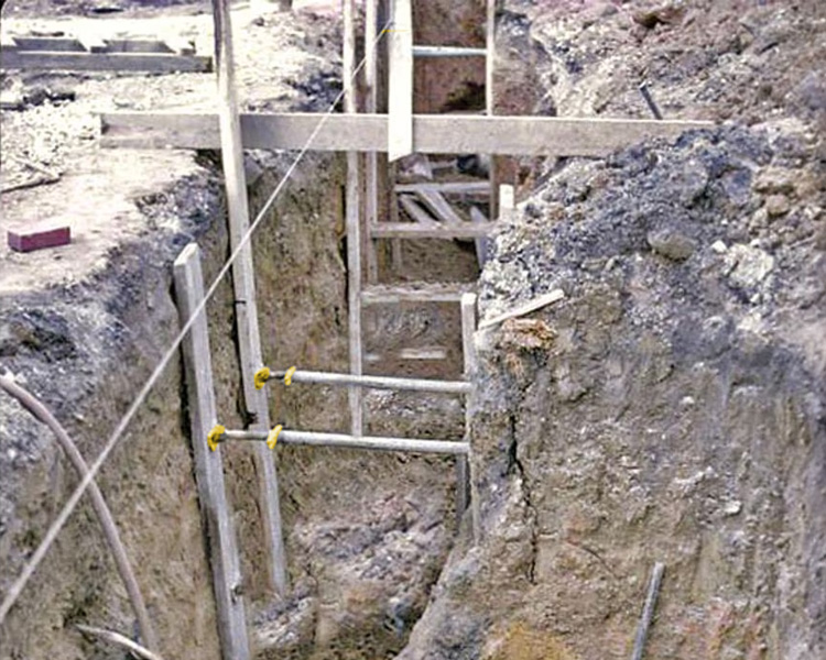 A construction worker wearing a hard hat, safety vest, and tool belt stands confidently next to a yellow featherlite ladder in a bright indoor setting.